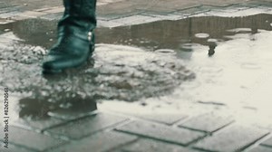 Person with high leather boots steps into a puddle of water.