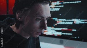 Close up shot of concentrated young male hacker coding on computer in dark office