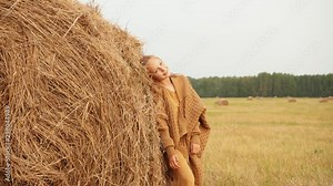 Fashion girl posing on haystack background on harvesting field in countryside. Young teenager girl leaning on dry haystack on rural field in village
