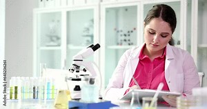 Scientist looks into microscope and writes medical report. Laboratory research in chemical liquids