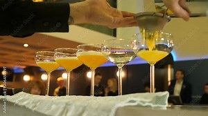 The barman pours a ready-made non-alcoholic cocktail in five glasses standing on the bar counter, a non-alcoholic cocktail based on citrus, mango and peach, moktel