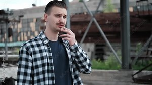young handsome man with mustache in checkered black and white shirt smoking a cigarette outside. bad habit.