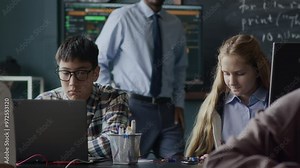 Multiethnic teenage students sitting at their places in modern classroom using laptop computers and assembling circuit boards during programming and engineering lesson with Black male teacher