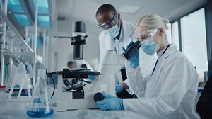 Modern Medical Research Laboratory: Two Scientists Wearing Face Masks Working Together Using Microscope, Analysing Samples, Talking. Advanced Scientific Lab for Medicine, Biotechnology. Side View Shot
