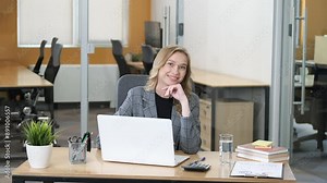 Beautiful young businesswoman sitting at table in office. Woman smiling while working in her laptop in a modern office.