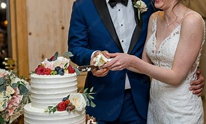 Wedding Celebration: A mid-shot of a bride and groom laughing together as they cut the wedding cake, with the bride playfully holding a piece of cake near the groom’s mouth.