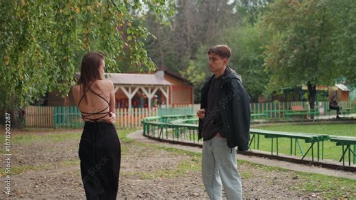 farewell at park bench shows hesitant distance and quiet reflection as couple faces choice leafy path, cabin backdrop, and scattered picnic tables frame moment of pause, phone glance, and turning