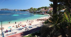 Beach promenade in the Beaulieu-sur-mer village with palm trees, pine trees and azure clear water, French riviera, France