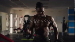 Front view concentrated sportsman lifting heavy dumbbells perspiring in gym indoors. Live camera zoom out and zoom in as strong African American athlete working out. Weightlifting and bodybuilding