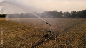 High angle aerial shot of field irrigation system watering crops. Arc of water seen from up close. Drone footage of farm spray head shooting water a long distance.
