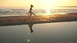 Young woman in white dress dancing on beach at evening time
