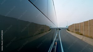 Side view of a public bus, shuttle, or school bus driving and the road reflection on it next to a cement barrier driving on the highways