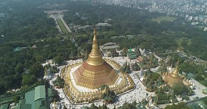Aerial drone view at Shwedagon Pagoda, a golden stupa, surrounded by lush greenery and urban development in Yangon (Rangun), Myanmar (Burma), showcasing the city's blend of religious and modern life.