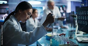 Biotechnology Research Laboratory: Two Caucasian Doctors Discussing CT Brain Scan On Computer. Focus Shifting to Female Asian Scientist Working With Test Tubes To Study Innovative Alzheimer's Medicine