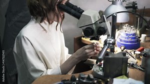 Side view of a woman jeweller examining a ring under a microscope. Tilt up real time medium shot Stock Video