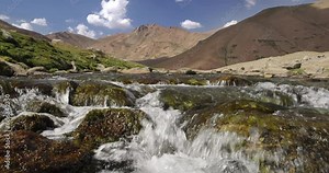 Mountain spring river water flows through hills. Strong brisk current of water flowing down in small waterfall from rocks against of hills. Mountain spring crystal clear water source of drinking water