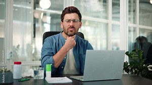 Ill businessman male manager has sore throat, clenches his hand into a fist and coughs close up. First symptoms of cold and flu virus, cough appeared. Man covers mouth face hands at workplace indoor.