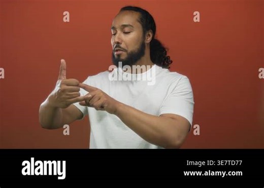 Man making call gesture with hand in studio against orange backdrop wearing white tee and beard; playful friendliness Stock Video Footage - Alamy