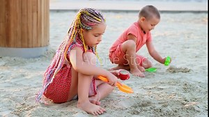 a child plays in the sandbox on the playground in summer, a little girl with bright pigtailed hair plays with sand on the beach and smiles, children's holidays