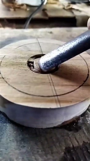 carving a circular groove into a flat wooden disc using a sharp metal chisel along marked pencil