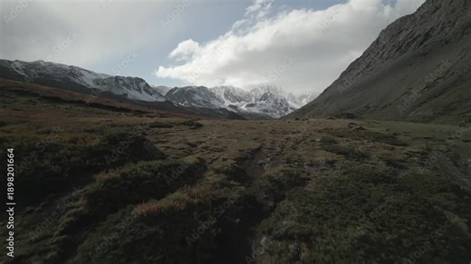 Raw unedited drone footage: aerial reveal shot flying past a hill to a deep mountain gorge. Scenic autumn landscape with colorful foliage and high peaks partially covered with snow.