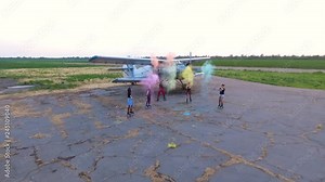 Cheerful young people throwing up colorful powder on an abandoned airfield, against the background of an old airplane. Aerial shooting.