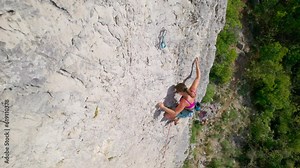 CLOSE UP: Sporty lady lead climbing a route in limestone wall above green trees. She climbs effortlessly and is advancing quickly on a sharp end of rope. Incredible climbing area in Karst landscape.