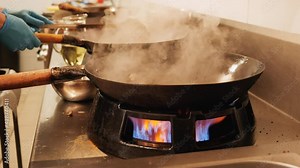 Chef working in restaurant kitchen handling the wok and stirring the food - preparing a delicious traditional asian meal