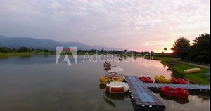 Tourist riding pedalo on recreational water park Aerial forwarding shot of people riding small colorful pedalo boats near floating dock during golden hour and reflected landscape on lake water surface