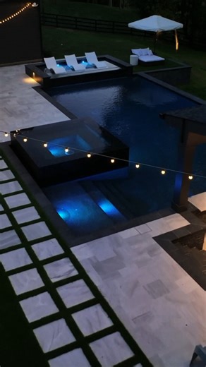 Georgia Classic Pool on Instagram: "This breathtaking backyard by Georgia Classic Pool proves that luxury truly shines after dark. Featuring sleek modern pool design, rich black glass tile, and a dramatic black pebble pool finish, this space transforms into a glowing nighttime oasis with stunning LED pool lighting. Unwind on the raised tanning ledge as soft landscape mood lighting sets the perfect ambiance. The experience is elevated even further with a modern cabana and outdoor kitchen, complet