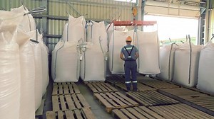 Worker Handling Large Bags in Warehouse, worker handling large bags in an industrial warehouse. The setting features heavy-duty equipment and pallets