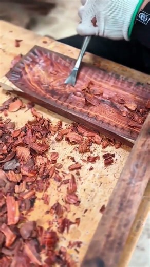 carving a textured pattern on a piece of dark wood with a sharp metal tool on a cluttered workbench