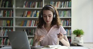Pretty teenage girl student sits at desk in library talks to tutor during remote online class, engaged in elearning, videocall event, studying using laptop. Education, modern tech usage, new knowledge