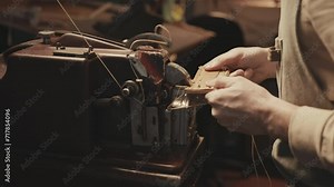 Hand of shoemaker using old-fashioned sewing machine for leatherwork in workshop