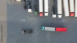 Aerial top down view of semi truck with cargo trailer moving along a warehouse with many containers standing on ramps for unloading and loading goods in a logistics park