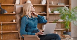 Focused mature woman typing on wireless laptop while sitting in comfortable armchair. Caucasian female psychotherapist using modern gadget for checking timetable.