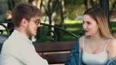 Young couple is sitting in a park on a bench, they are looking at...