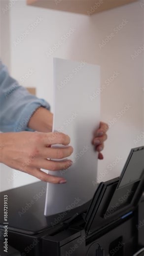 Close up of hands printing documents in home office inserting stack of blank white paper , remote work process with paperwork, laptop and printer, freelance administration and business routine
