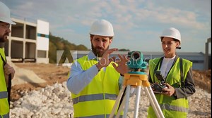 On project construction workers discussing and using theodolite surveying optical instrument for measuring. Group engineers standing at sunlight. Building company