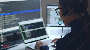 Asian woman developer programmer, software engineer, IT technical support wearing headsets talking with team, working overtime at night on computer to check coding bugging system. Back view