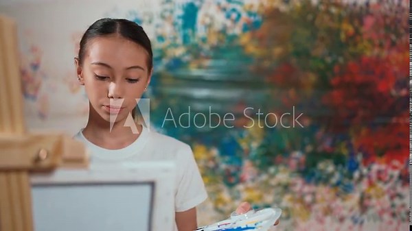 Pretty high school student painting canvas while standing at stained wall. Caucasian teenager use paint brush and palette to drawing a picture in art lesson. Creative education concept. Edification