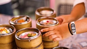 Hands arranging bamboo steamers filled with colorful dim sum on a table in Phuket, Thailand. Bright, natural lighting enhances the vibrant scene