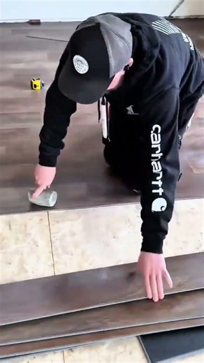 Worker carefully installing wooden floor planks using hammer to secure edges tightly in place