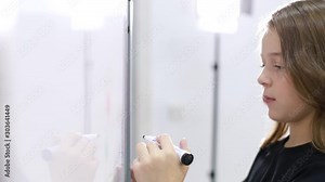 Little girl draws a marker on a blackboard at school. A clever child