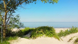 Panning view typical Baltic sea coast landscape beach view in Lithuania. Blue sky with no clouds, small waves in the sea and sand dunes partially overgrown with sedge grass