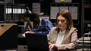 Focused female private detective using laptop to analyze confidential documents in criminal investigation. Caucasian investigator cross-checking crucial evidence and statements on personal computer.