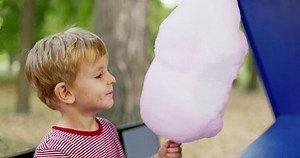 Little boy is eating pink cotton candy in the park