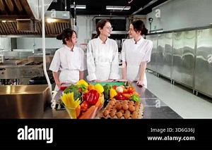 Chef instructor teaching two young culinary students in a commercial kitchen during a professional cooking class with fresh vegetables. Ideal for chef training, gastronomy, and food education themes.