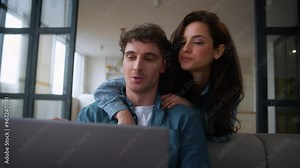Caucasian woman female girl wife girlfriend hugging man back discuss shopping computer talk choose purchase order delivery tickets booking laptop man male guy boyfriend husband couple talking home