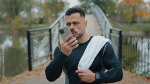 Sportive Caucasian Man Walking in the Park with Towel on his Shoulder, Recording a Voice Message to Share his Sport Results after his Outdoor Run. Finishing his Workout and Enjoying the Fresh Air